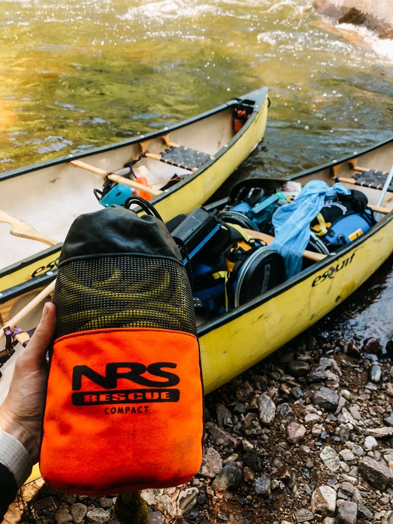 Hand holding an NRS throw bag over a yellow canoe on a river