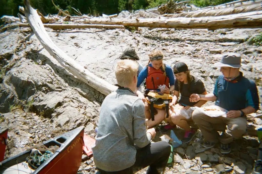 Group of teenagers preparing wraps, a common canoe camping meal, on the shore.